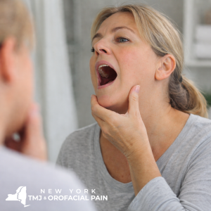  Woman gently opening jaw to assess TMJ symptoms related to connective tissue disorder or arthritis